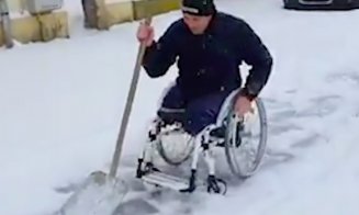 Bărbat în scaun cu rotile, cu picioarele amputate, surprins dezăpezind un trotuar